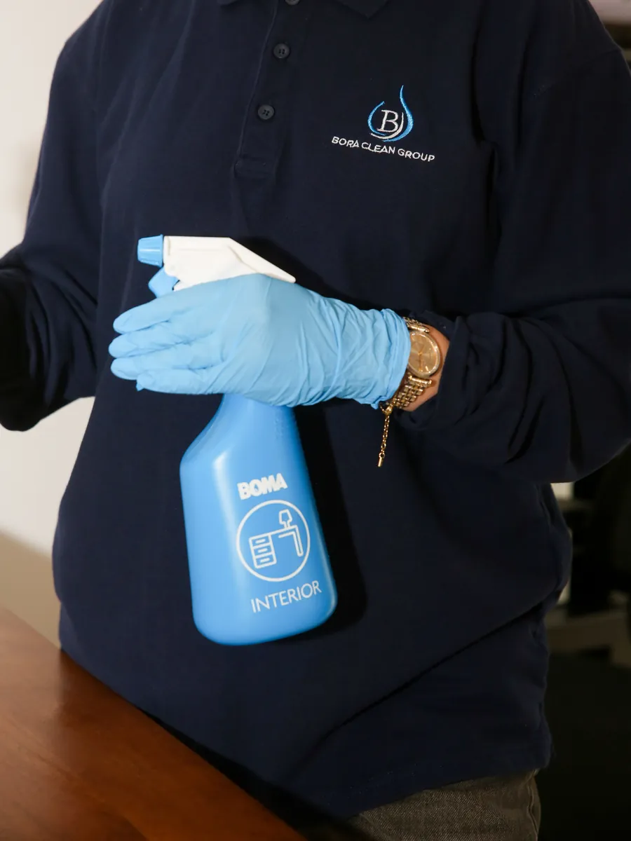 Agente Bora Clean en polo, un vaporisateur BOMA Interior à la main, près d'un bureau