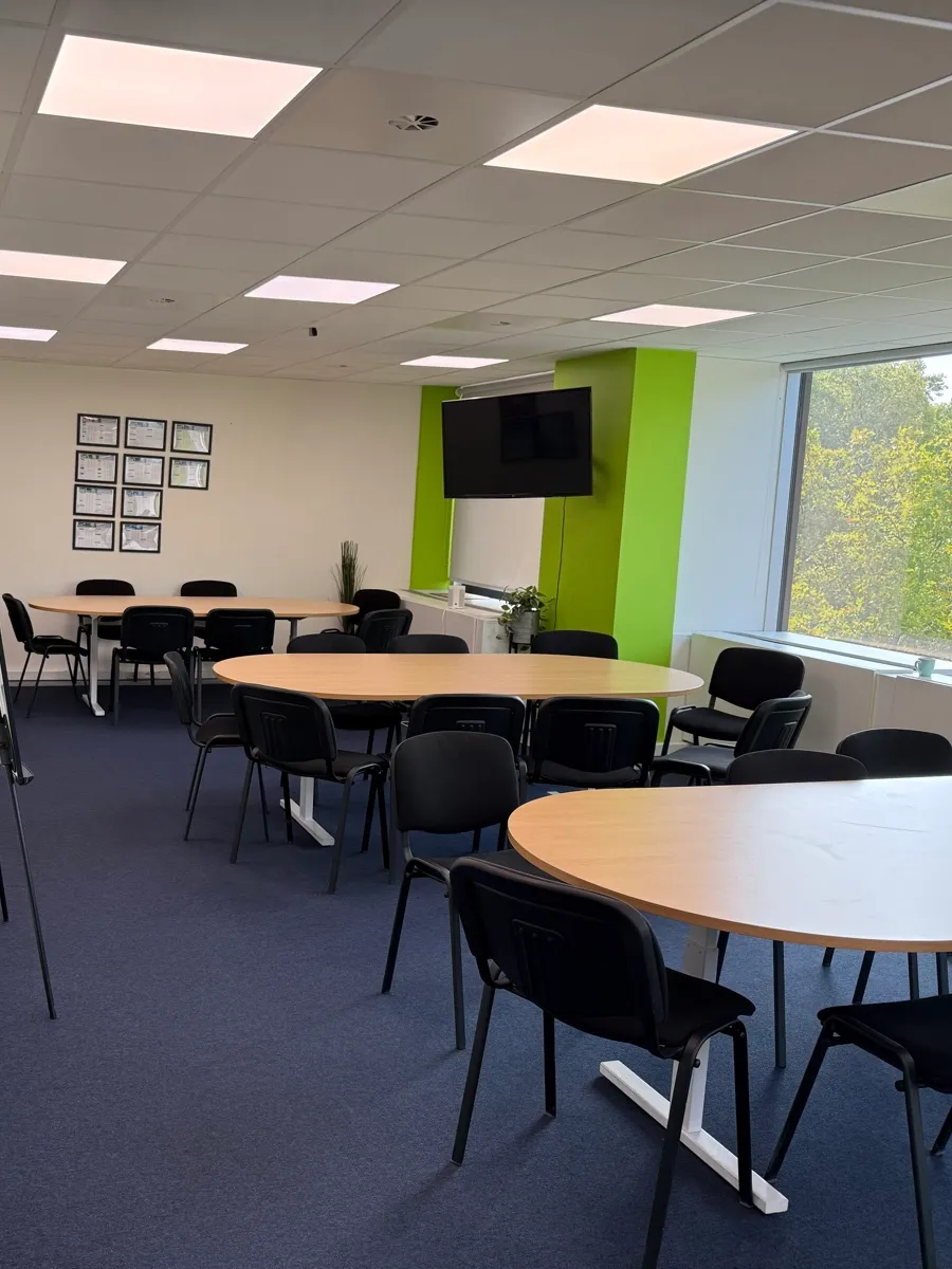 Salle de réunion claire : tables ovales, chaises rangées, écran au mur et grande fenêtre