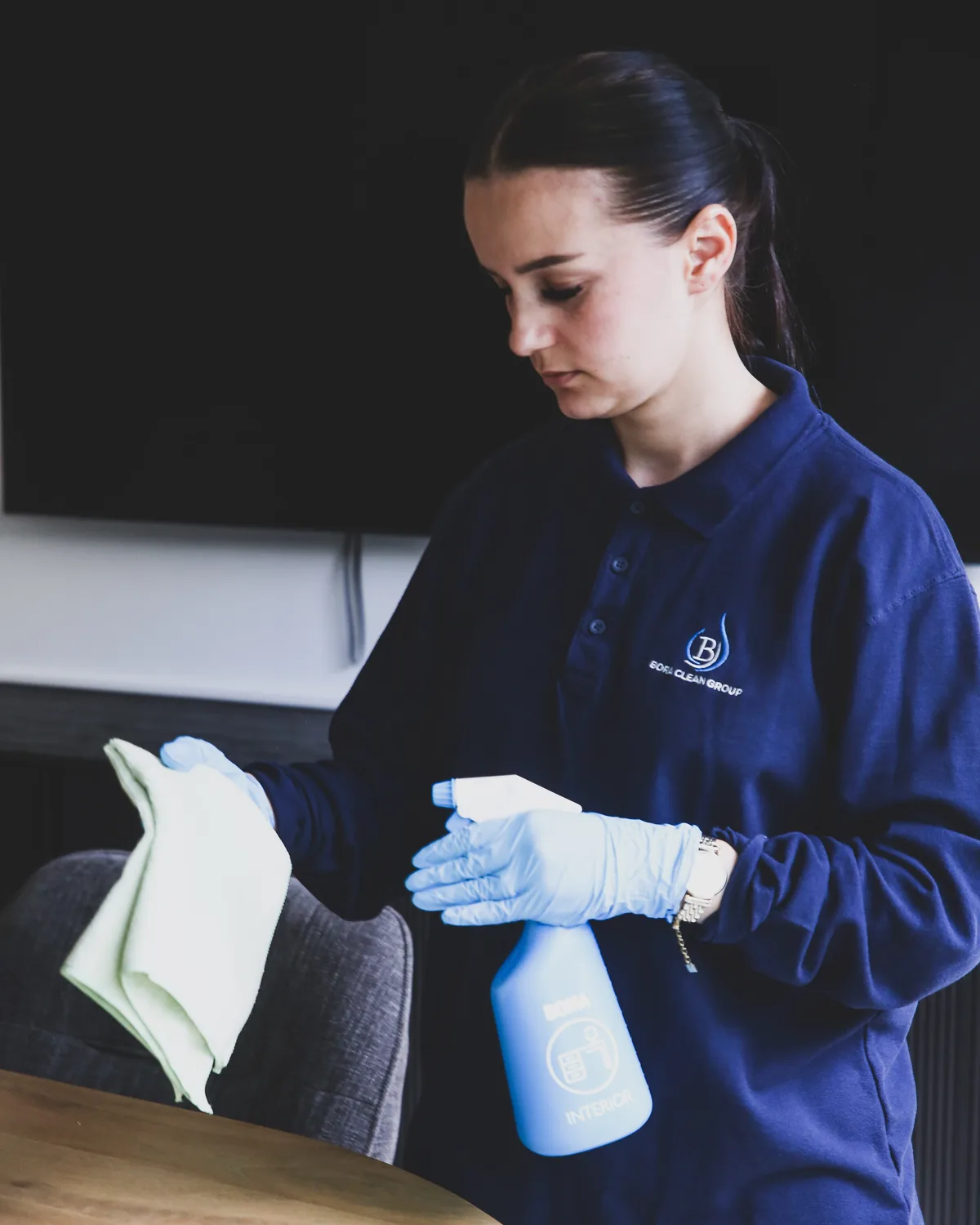 Een medewerkster van Bora Clean in werkkledij ontsmet een vergadertafel