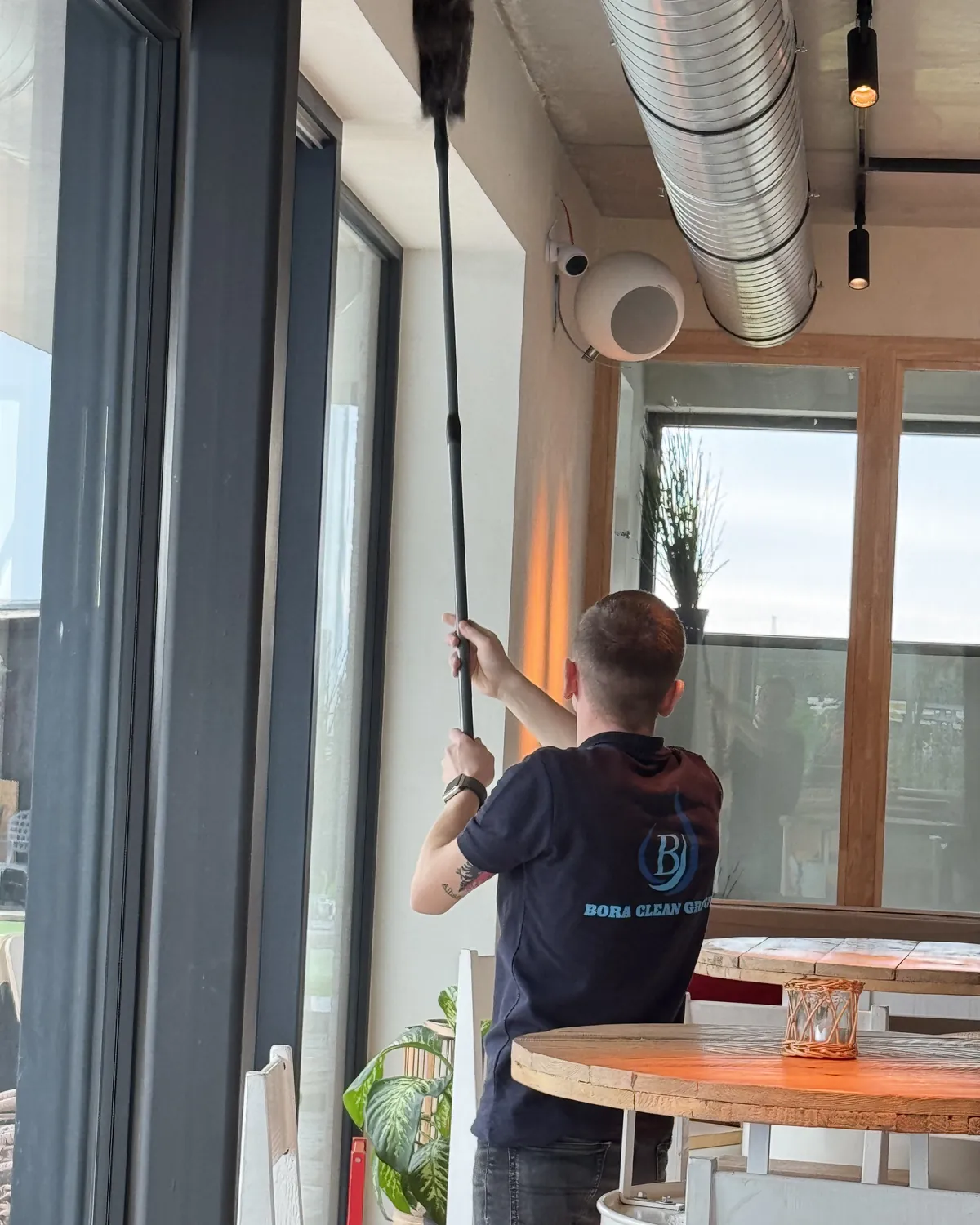 Een medewerker van Bora Clean Group stoft met een lange steel de bovenkant van een grote raampartij af