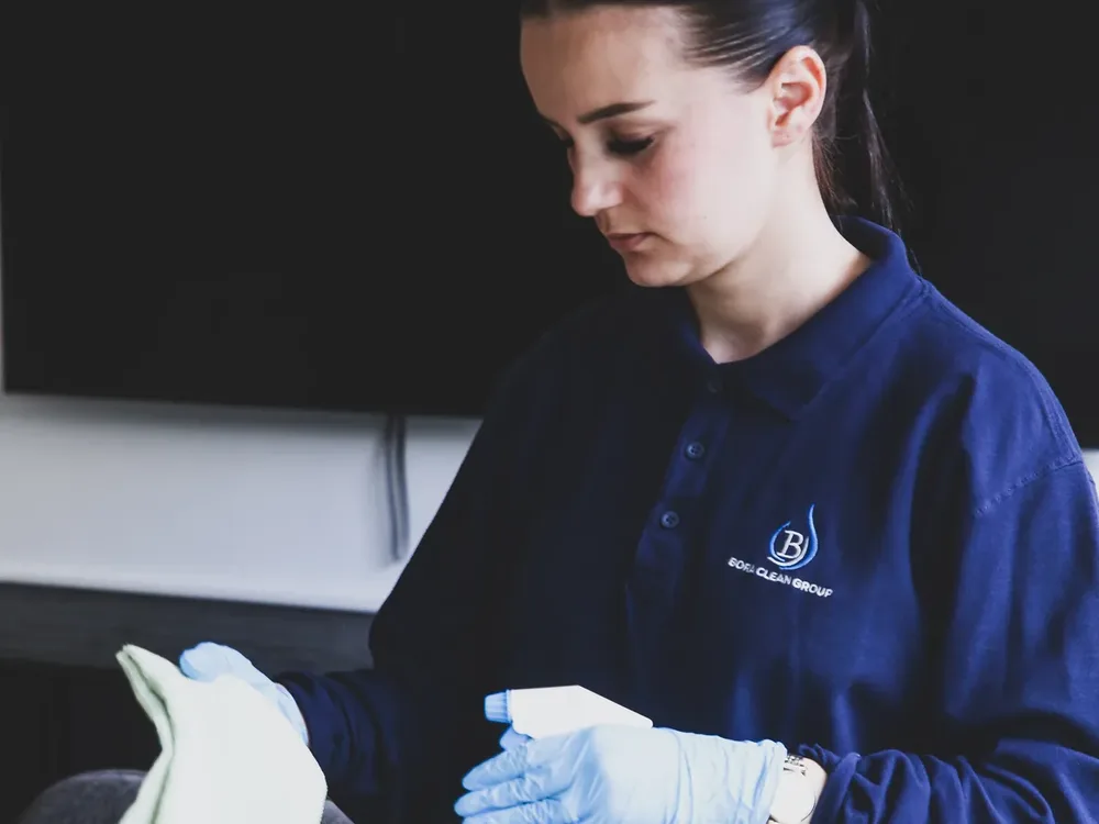 Une agente Bora Clean Group en tenue de travail, gantée, un chiffon et un vaporisateur en main