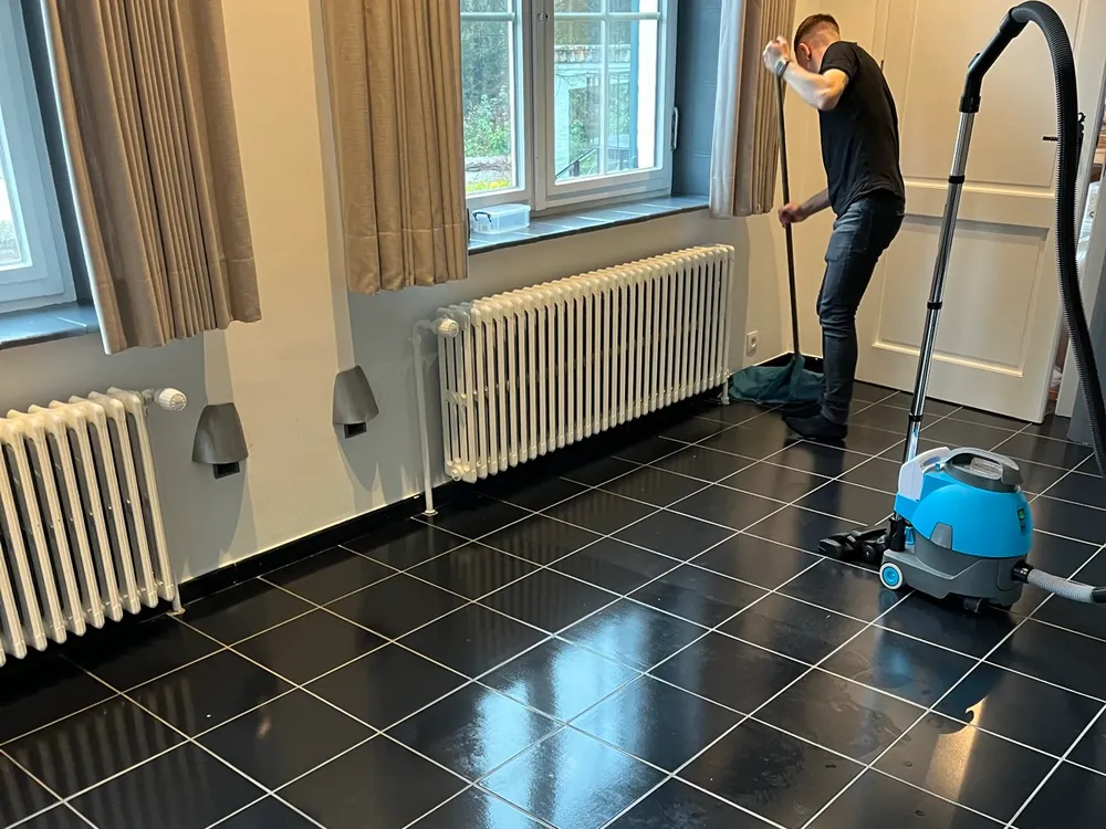 Un agent Bora Clean Group nettoie un sol carrelé noir et brillant, l'aspirateur à ses côtés