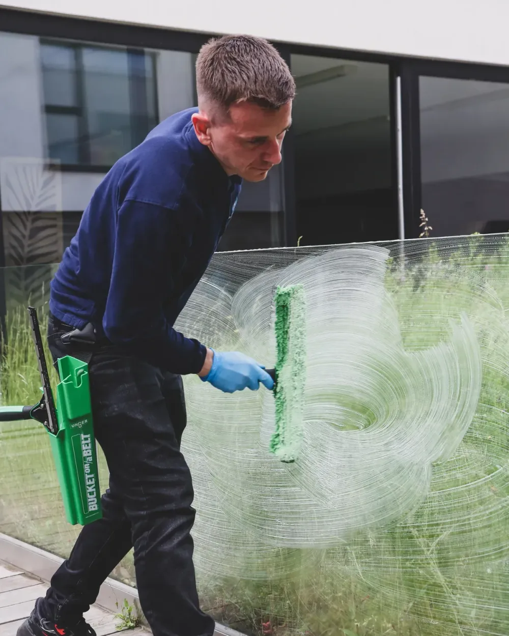 Een medewerker van Bora Clean wast een glazen balustrade met een inwasser, op het terras van een kantoorgebouw